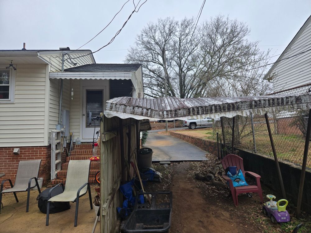 Backyard with porch, chairs, fence, icicles hanging from a roof, car in driveway, overcast sky.