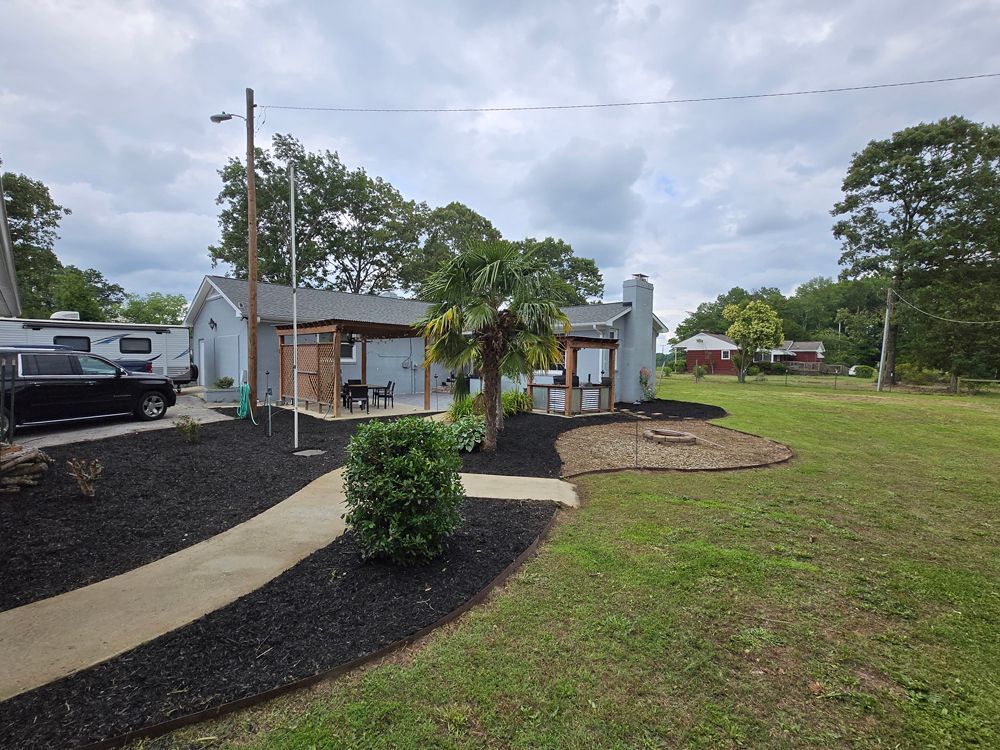 House with dark mulch landscaping, concrete path, and an RV parked outside.