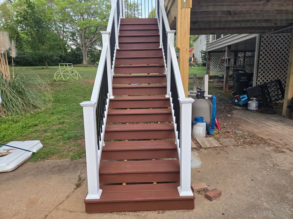 Outdoor staircase leading to a deck, brown steps, white and black railing, concrete base, grassy yard.
