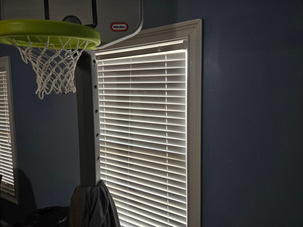 A basketball hoop hangs near a window with white blinds in a blue-walled room.