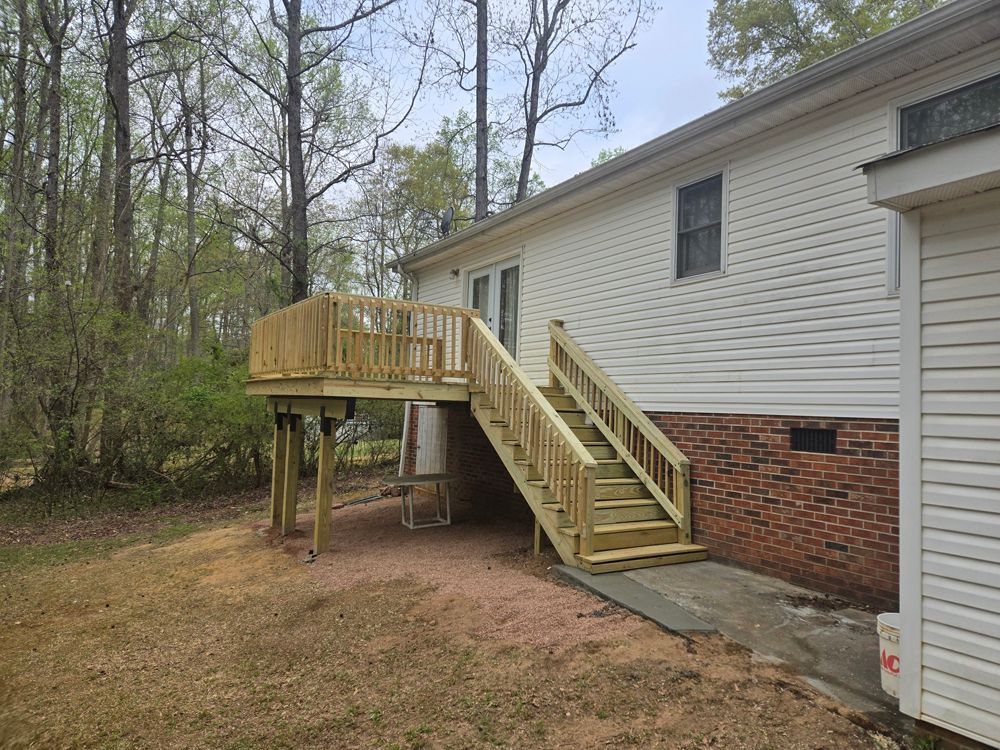 Wooden deck with stairs attached to a white house, set in a backyard with trees.