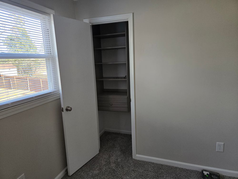 Bedroom with open closet, window, and gray walls and carpet.