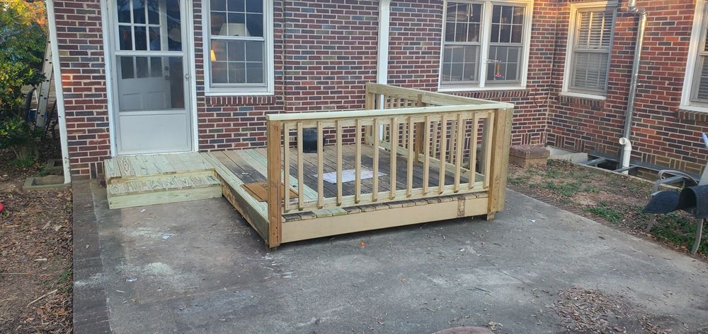 Wooden deck construction against a brick building with a door and windows.