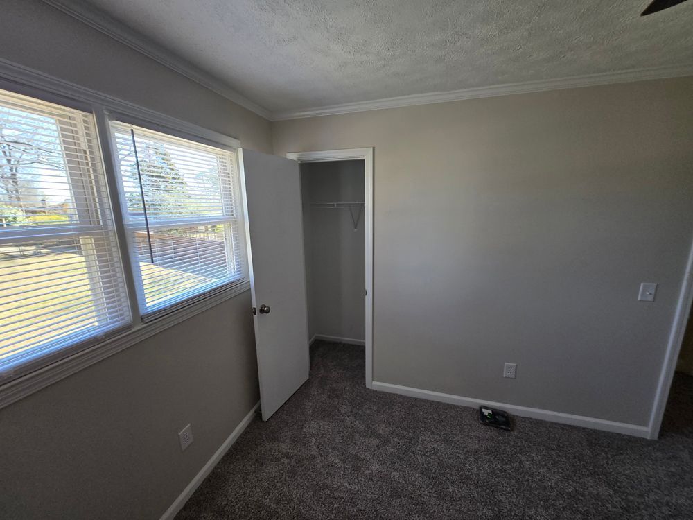 Empty bedroom with gray walls, closet, windows, and carpet.