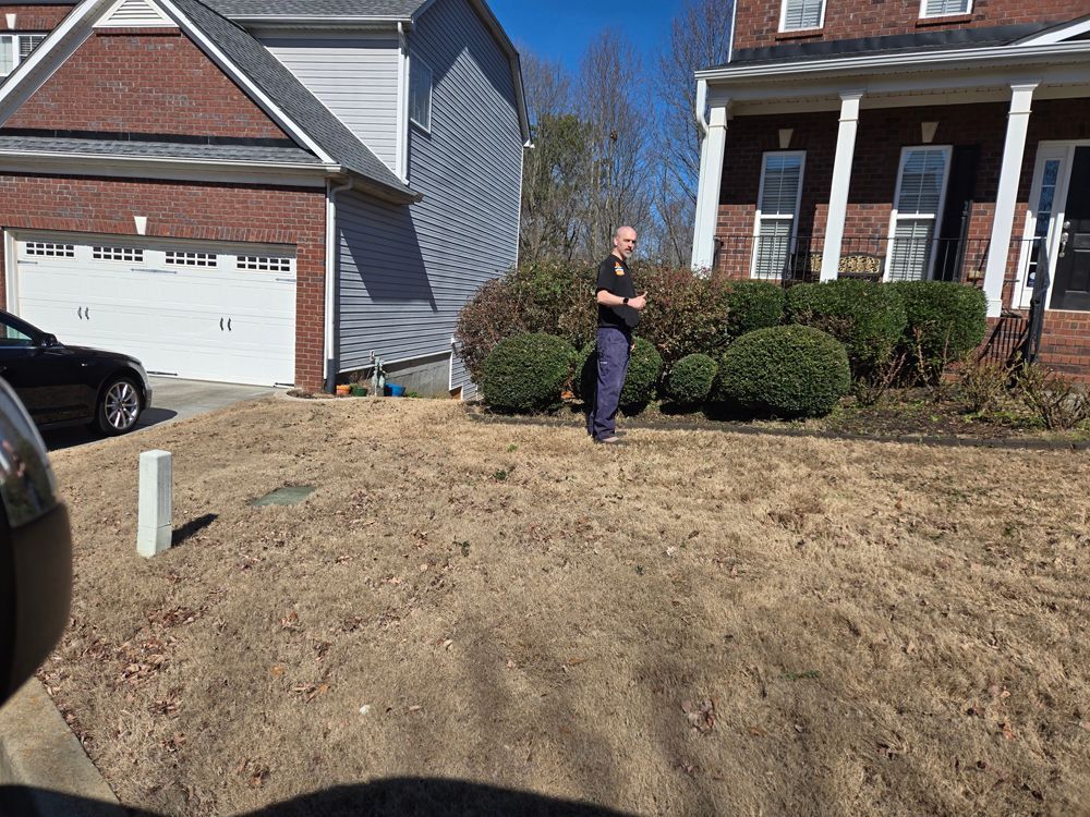 Man standing in a brown yard in front of two houses on a sunny day.