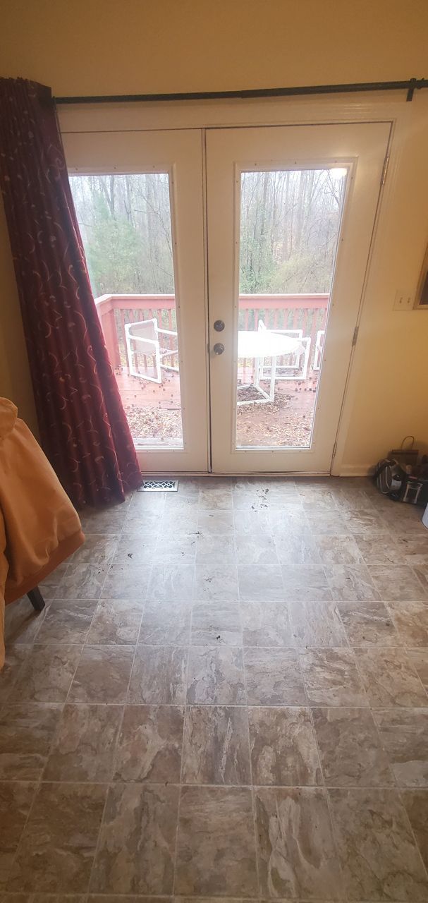 French doors open to a deck with white furniture, burgundy curtain, and patterned flooring.