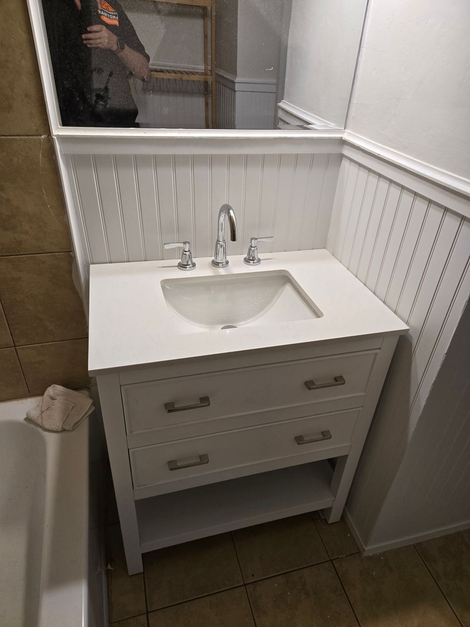 White bathroom vanity with two drawers, a sink, and a mirror, set against a beadboard wall.