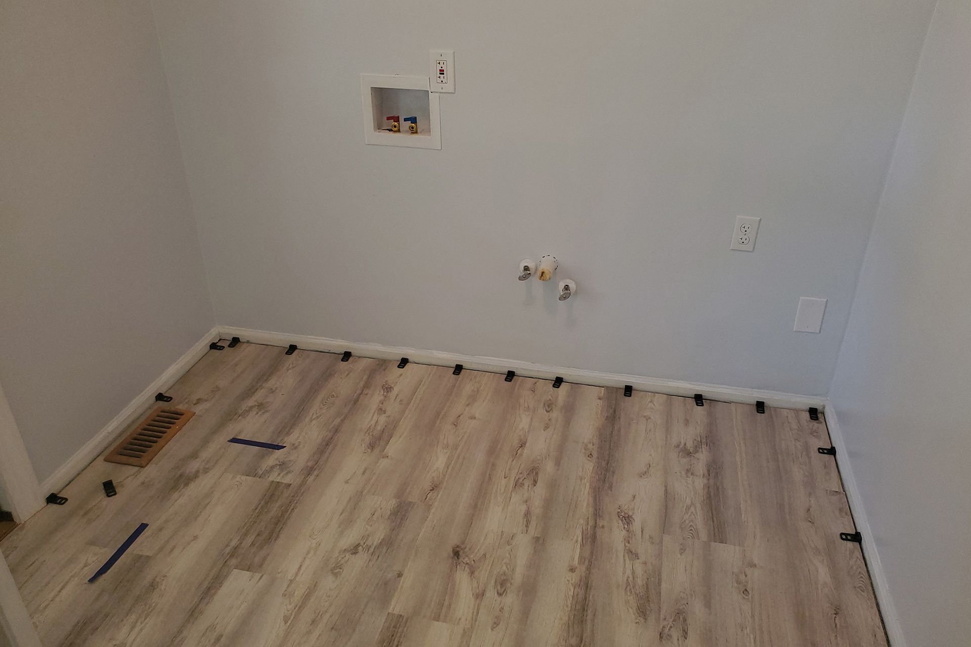 Laundry room with new wood-look flooring, white walls, and utility hookups.