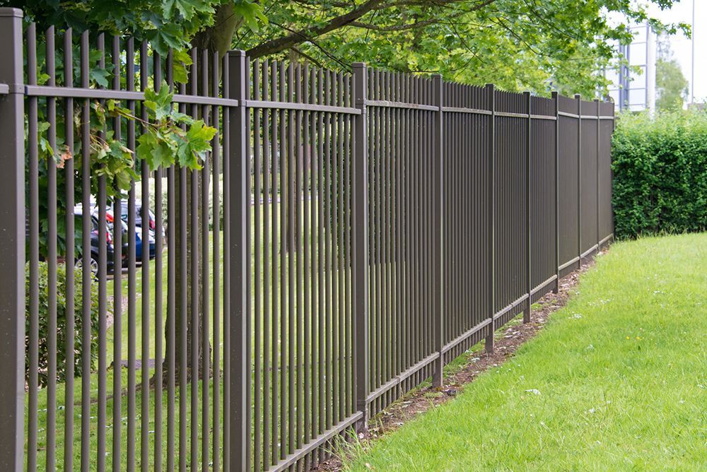 Brown metal vertical bar fence bordering a grassy lawn.
