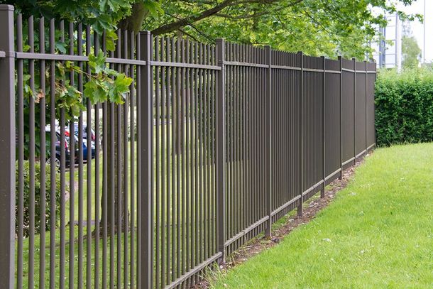 Brown metal vertical bar fence bordering a grassy lawn.