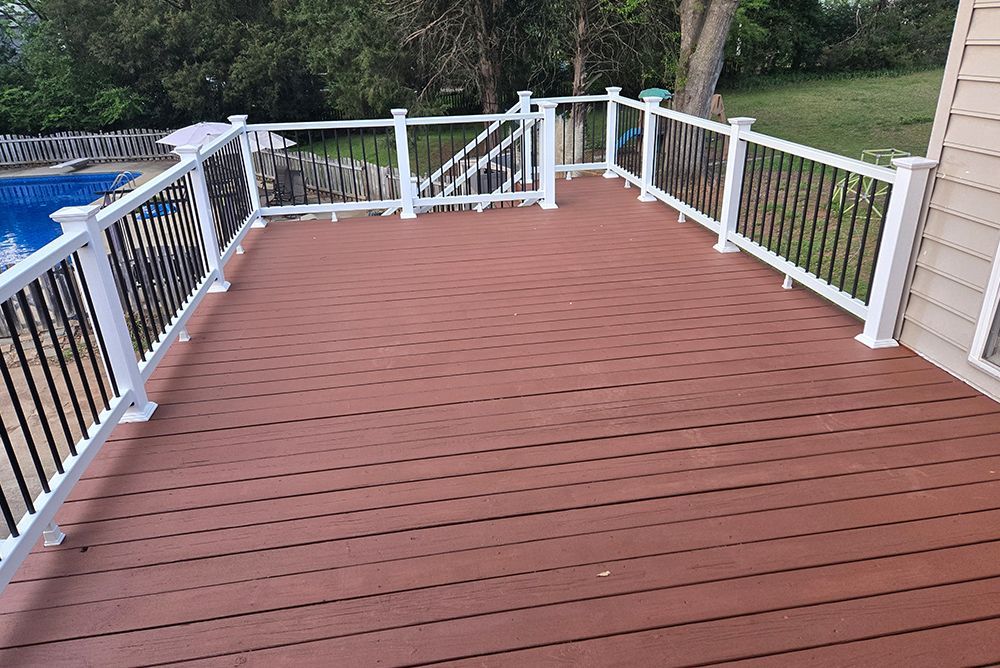 A wooden deck with white railings and black balusters; a pool is in the background.
