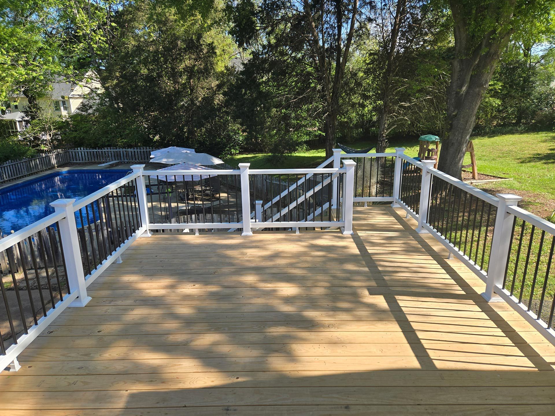 Wooden deck with white railing, black spindles, overlooking a blue-covered pool.