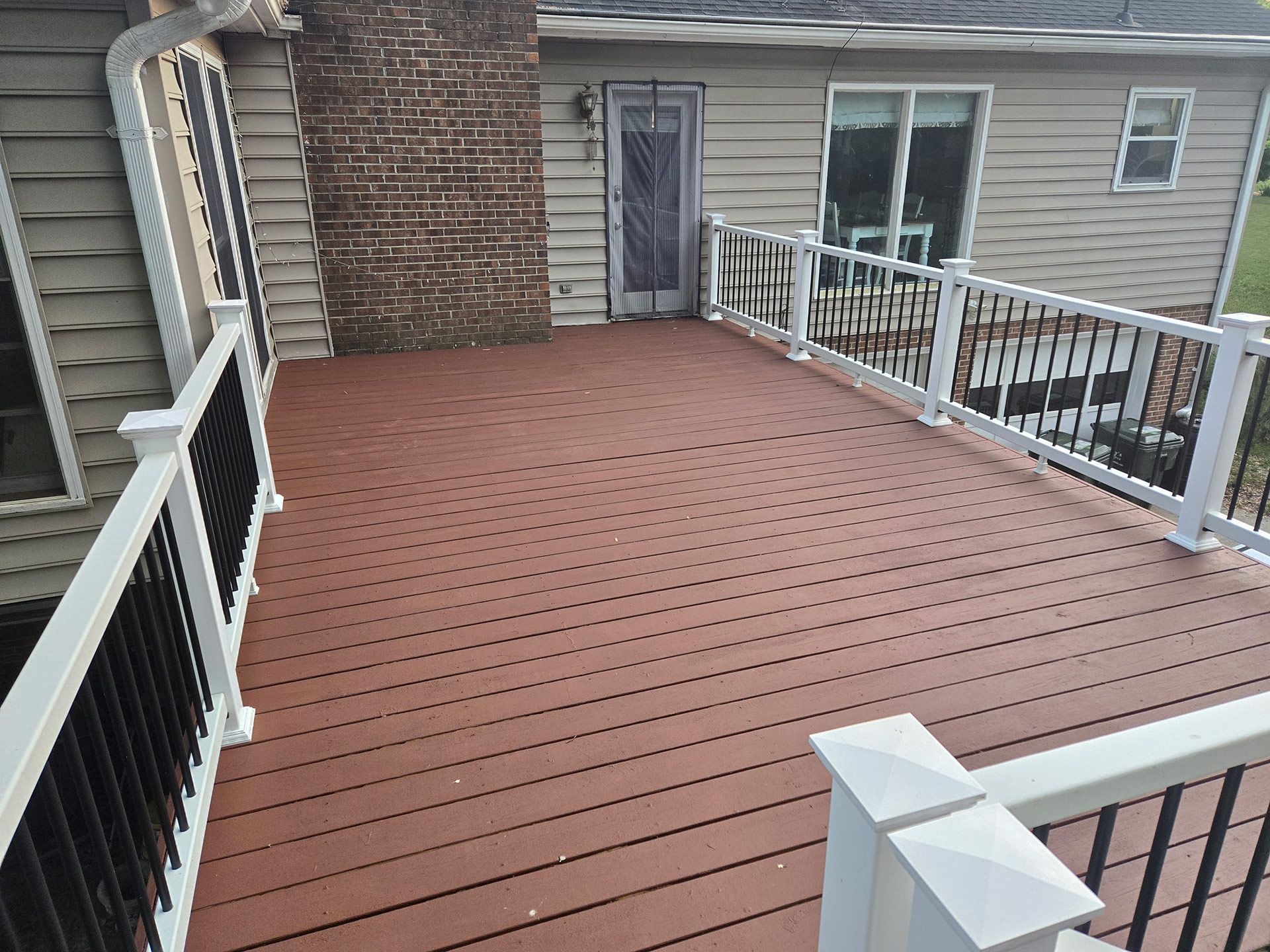 Brown composite deck with white and black railings next to a brick chimney and a house.