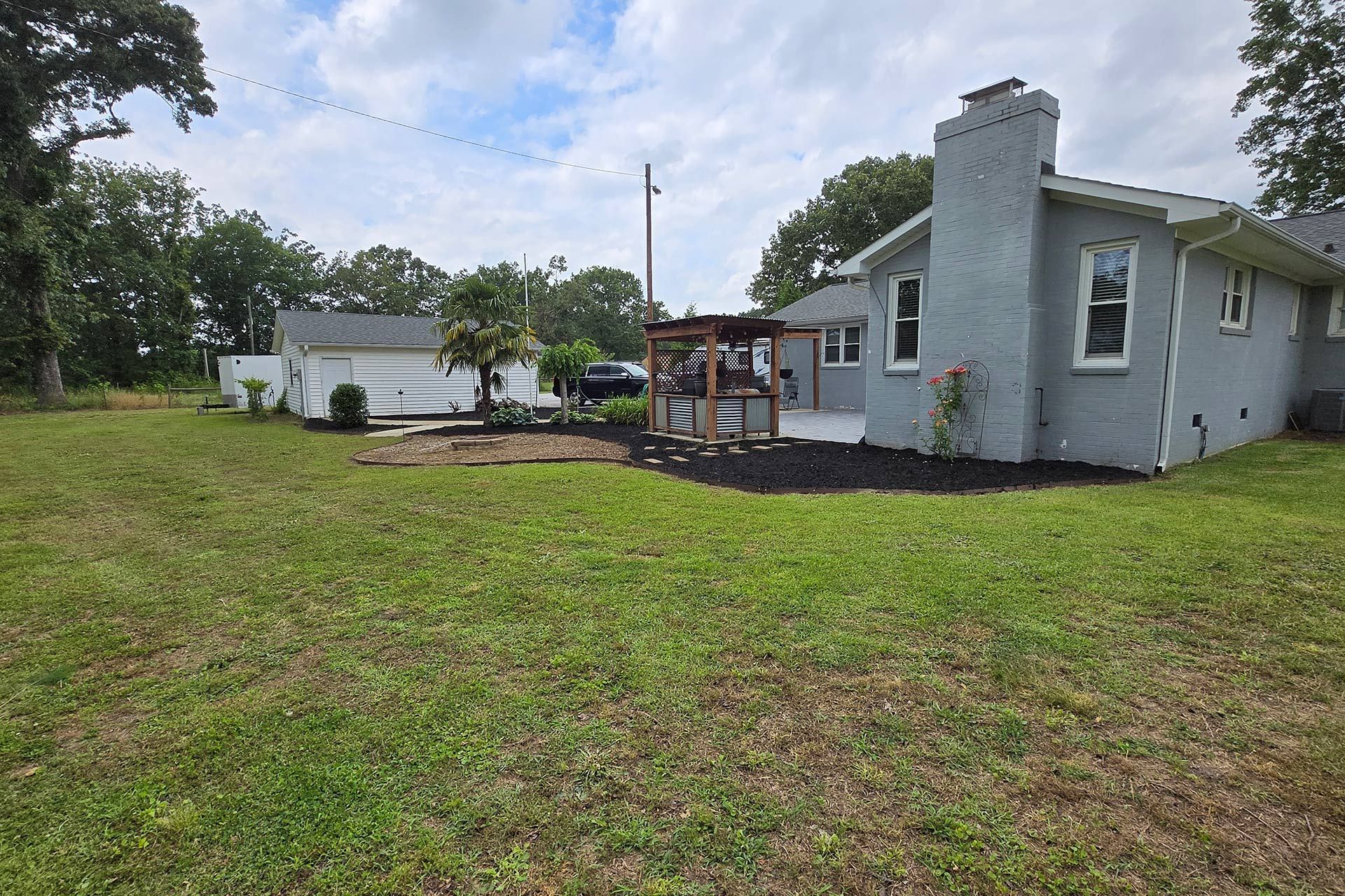 Backyard with house, patio, garage, and grassy lawn on a cloudy day.