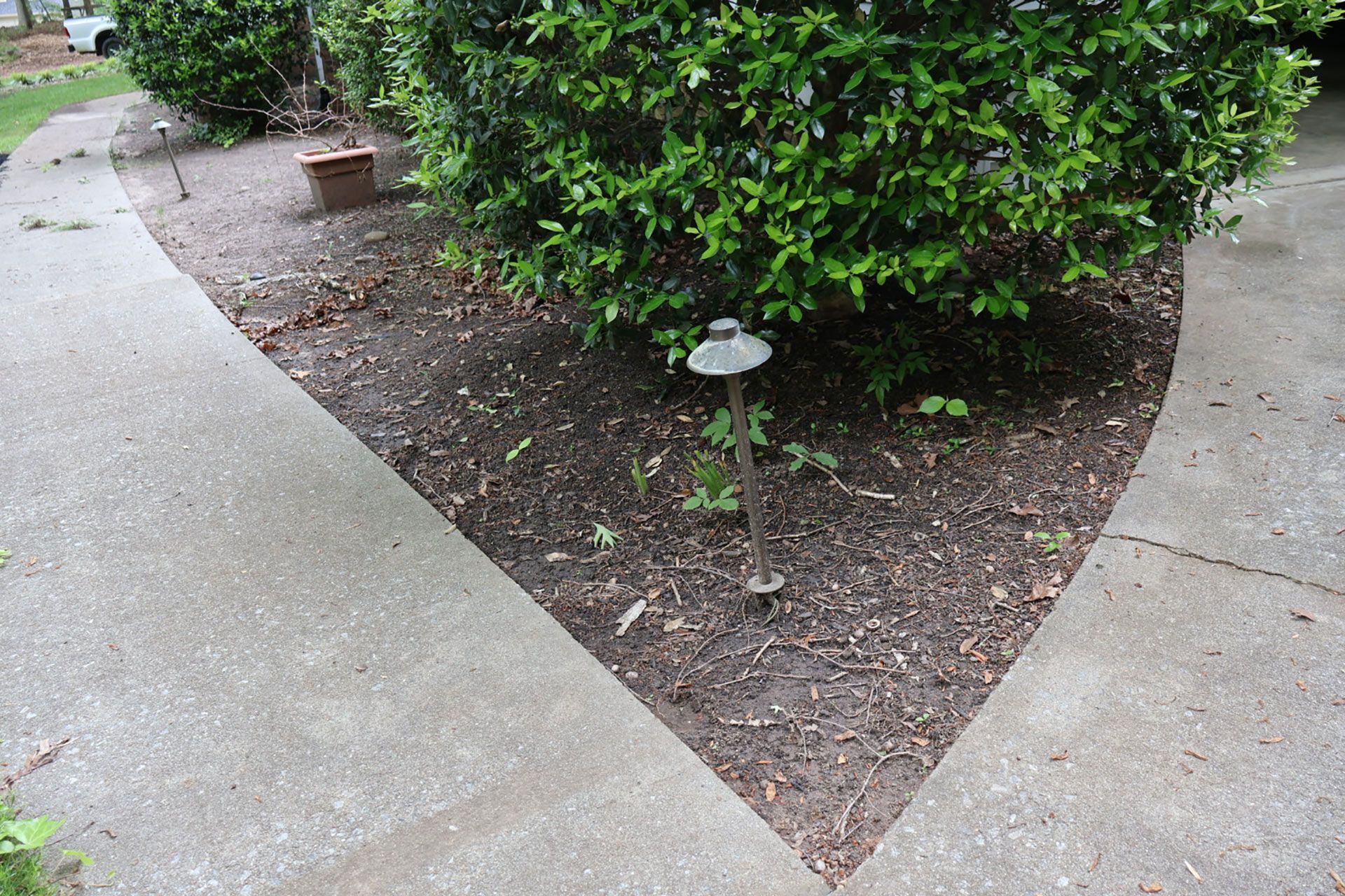 Concrete path curves around a shrub in a garden bed; a pathway light is visible.