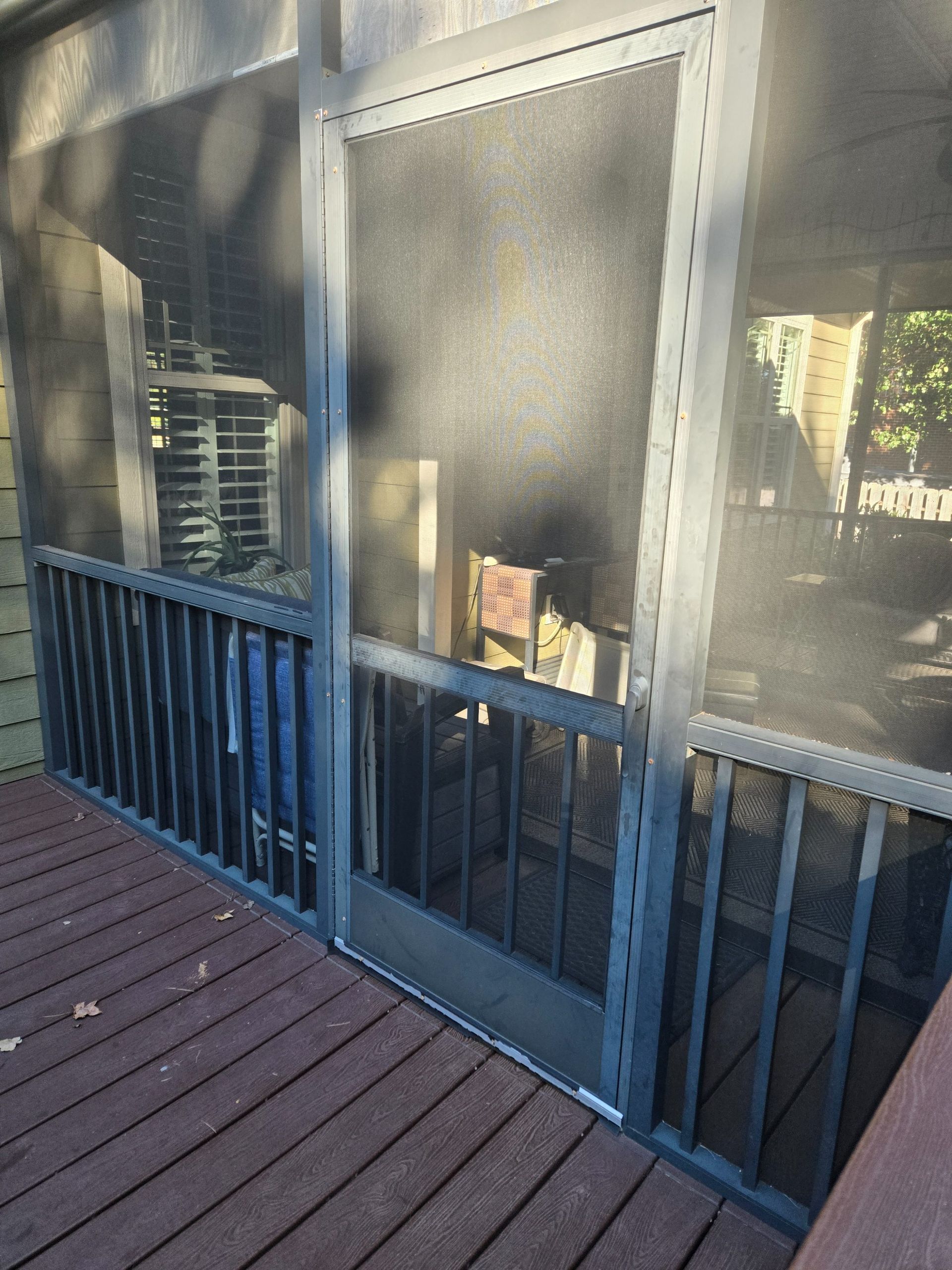 A dark gray screened-in porch with a central door and matching railing, viewed from a wooden deck in the evening.