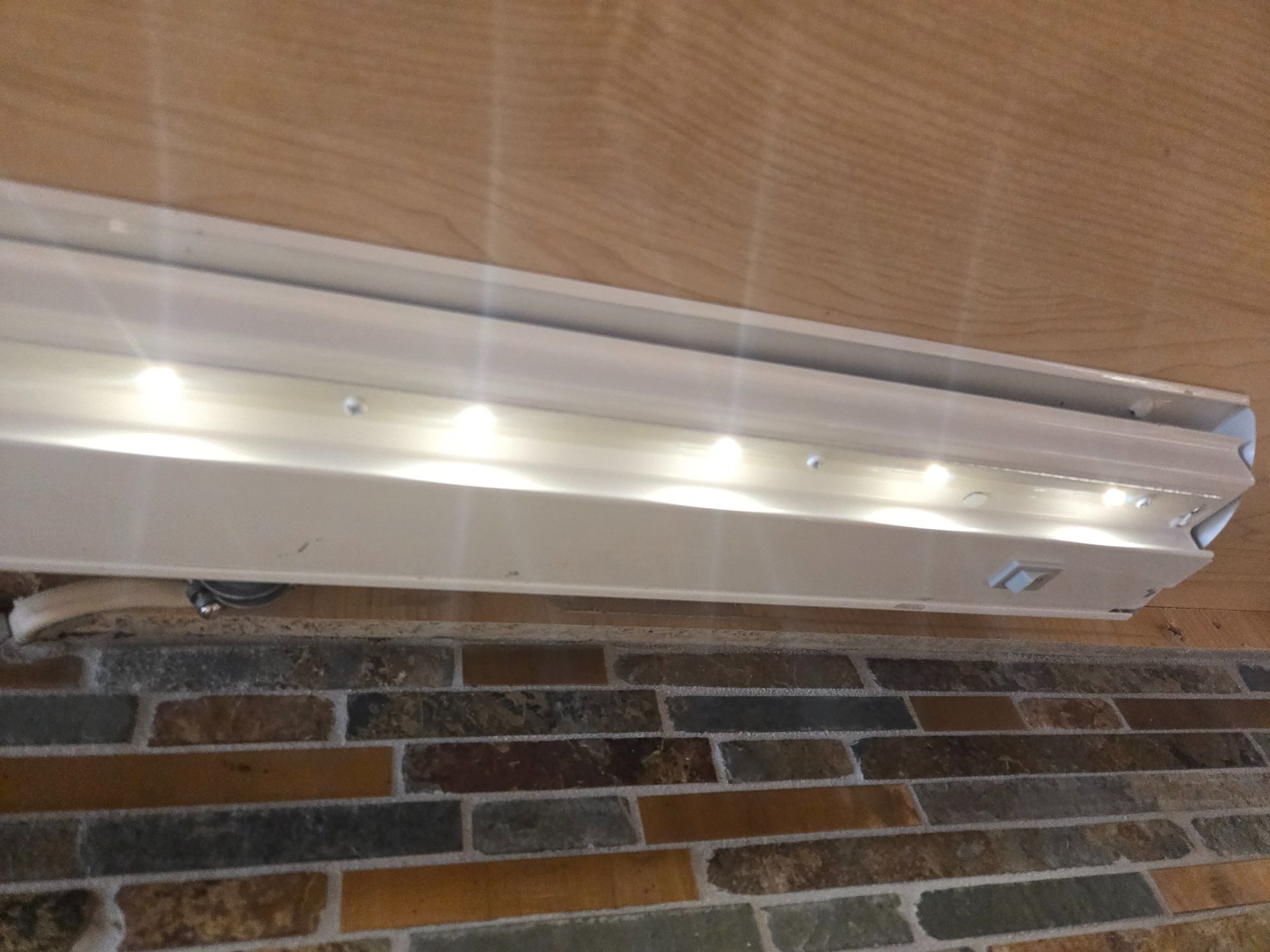 A long, white under-cabinet LED light strip mounted above a multicolored stone-patterned backsplash.