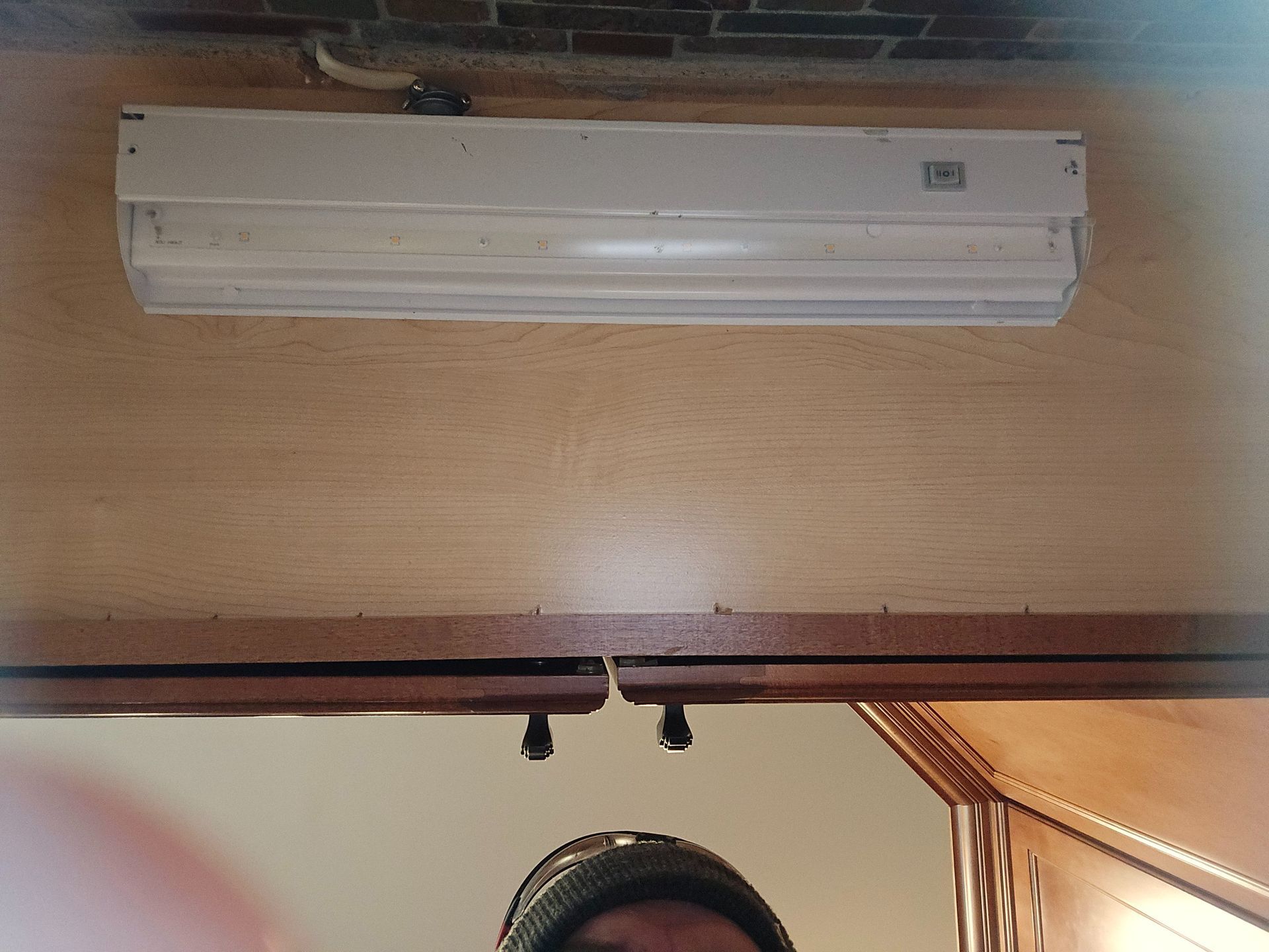 A white under-cabinet fluorescent light fixture mounted beneath a kitchen cabinet.