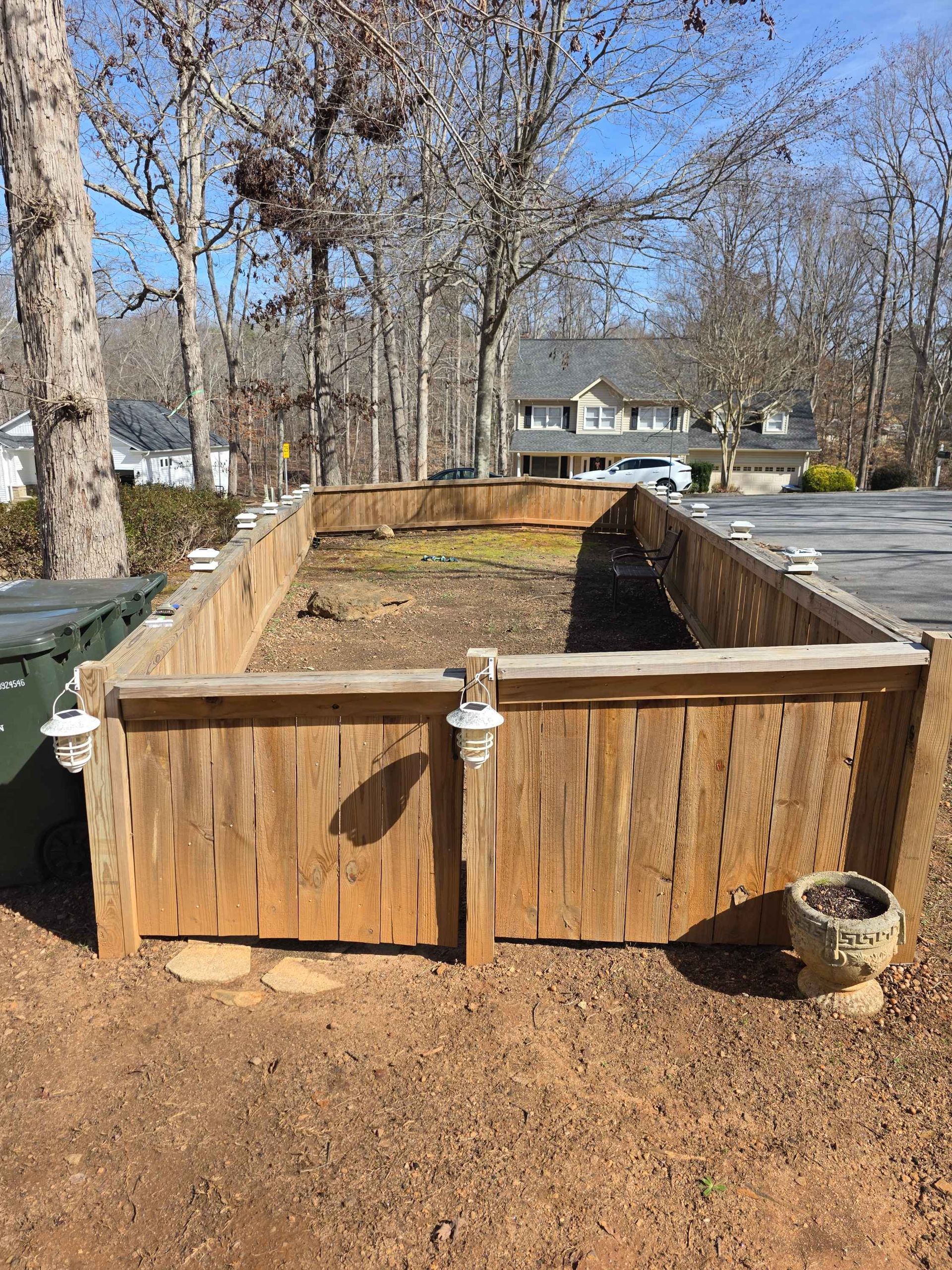 A rectangular wooden garden bed with solar lights on the posts sits in a yard in front of a house.