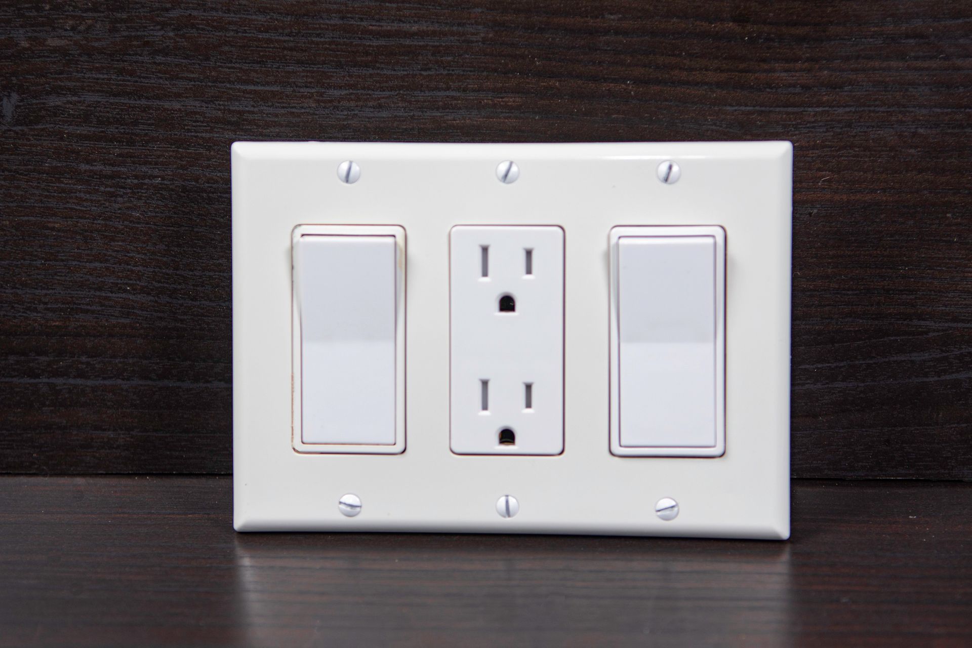 White light switch and outlet plate on a dark wooden background.
