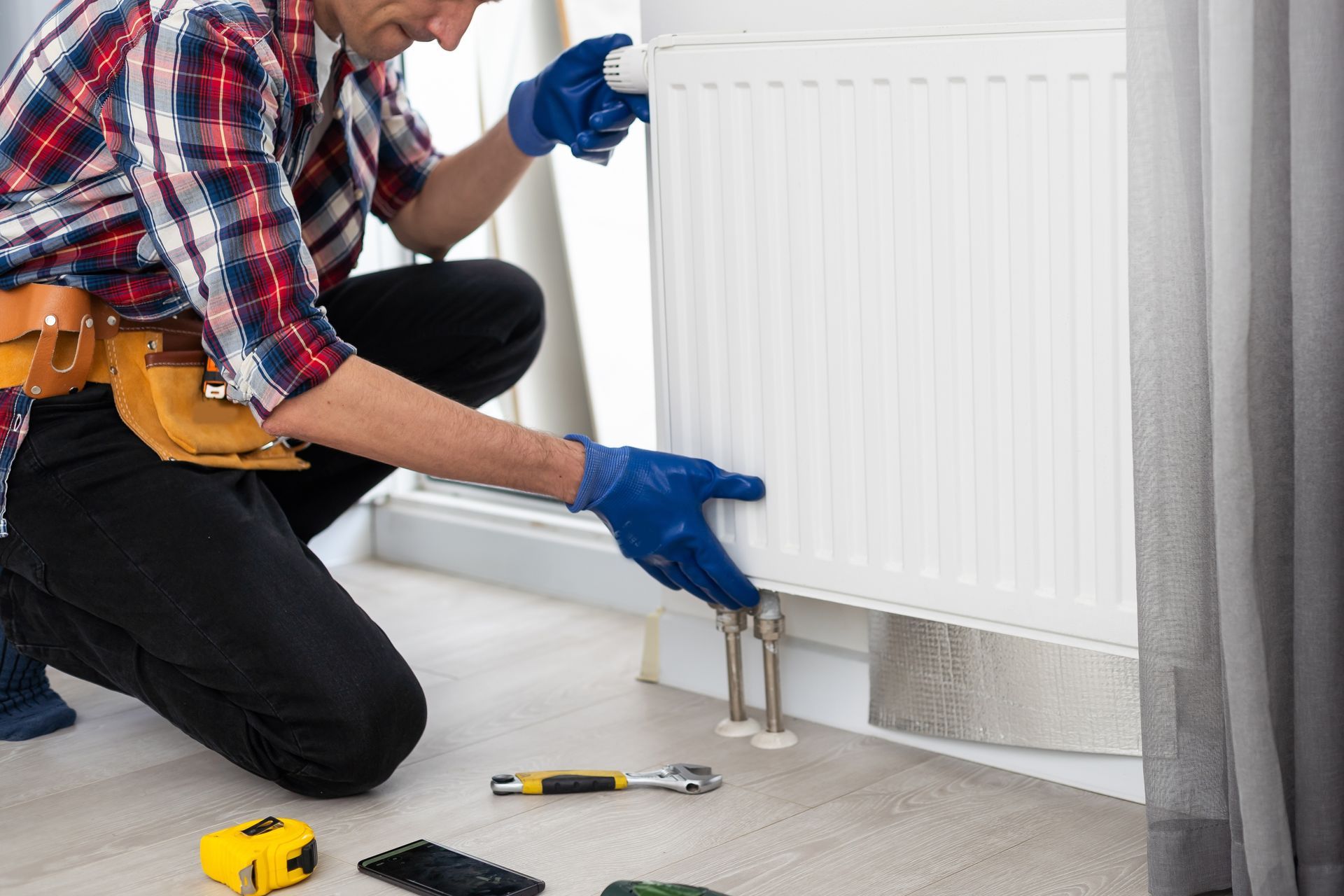 A man is kneeling on the floor fixing a radiator.