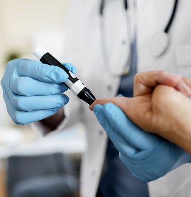 Gloved clinician using a lancet to test a patient’s fingertip blood sugar