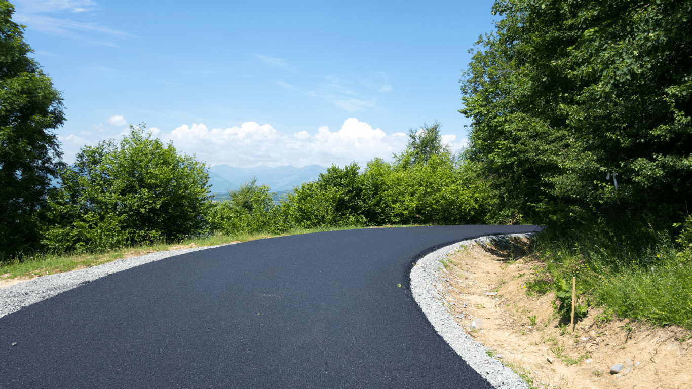 Newly paved asphalt road curving through a green landscape with trees and distant hills during an asphalt paving service in Highlands Ranch, CO