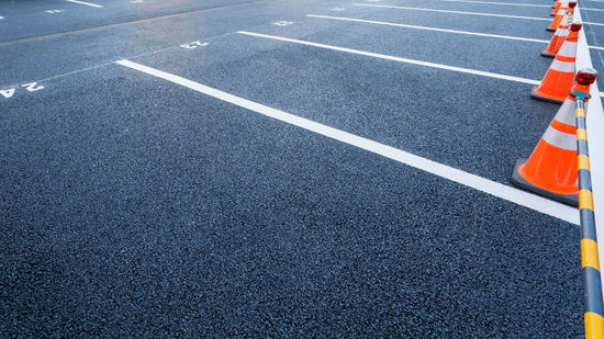 Freshly paved asphalt parking lot with bright white striping lines and orange cones marking spaces during an asphalt paving service in Highlands Ranch, CO