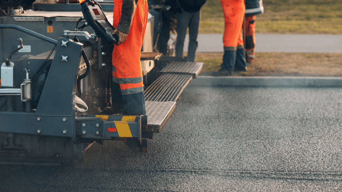 Workers standing on paving equipment as it spreads and smooths hot asphalt evenly across the surface during an asphalt paving service in Highlands Ranch, CO