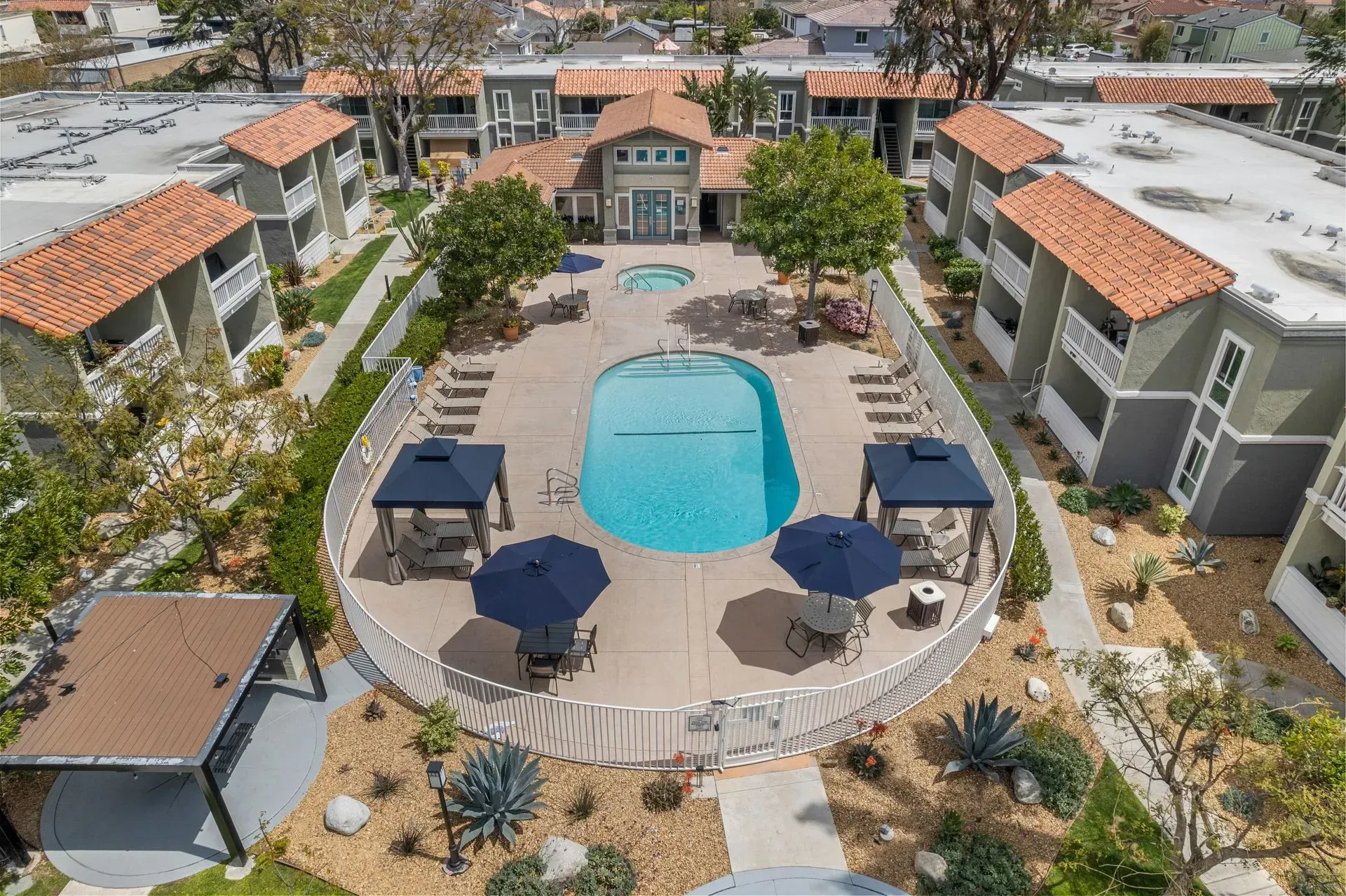 Aerial view of apartment complex with a pool, surrounding buildings, and landscaping.