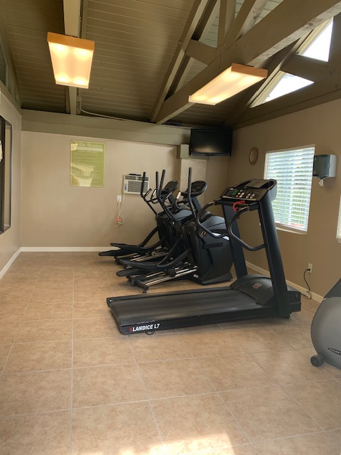 Gym with elliptical machines and treadmill; brown walls and tiled floor.