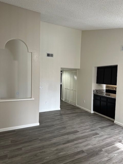 Empty living room with gray wood-look flooring, arched wall detail, and a doorway to a hallway with white doors.