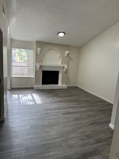 Empty living room with fireplace, gray flooring, window, and white walls.