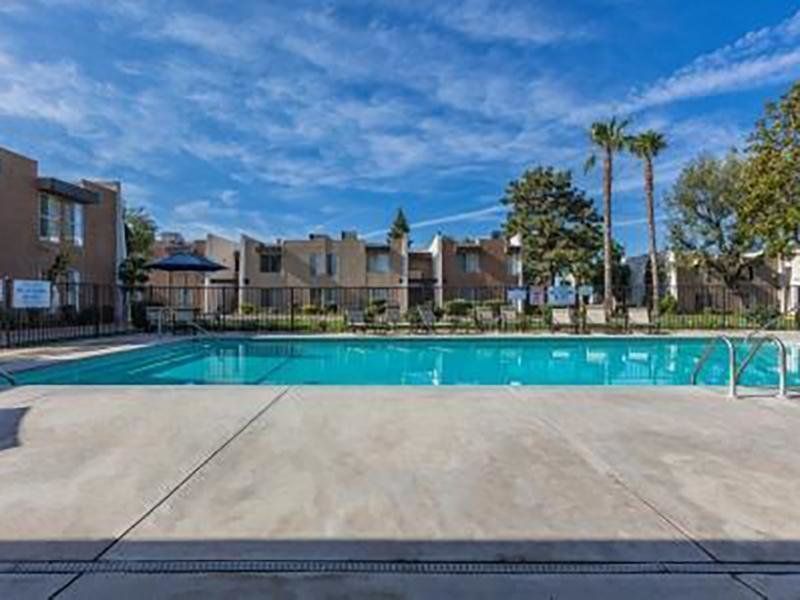 Swimming pool in front of apartments under a blue sky with palm trees.