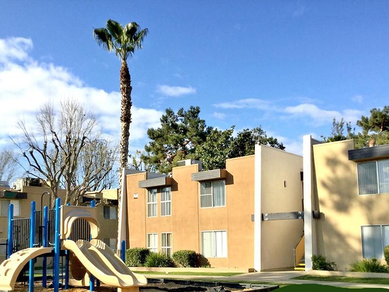 Apartment complex with playground and tall palm tree under blue sky.