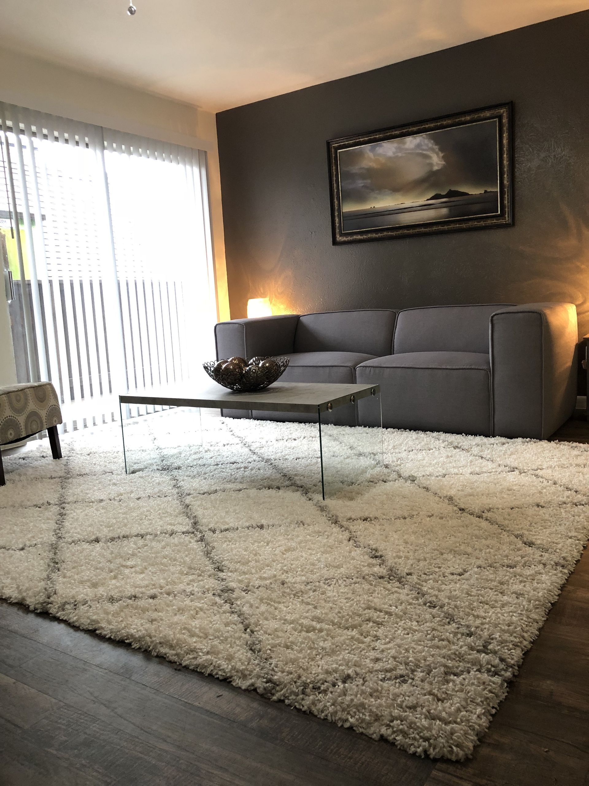Living room with gray sofa, white shag rug, and painting on a dark gray wall.