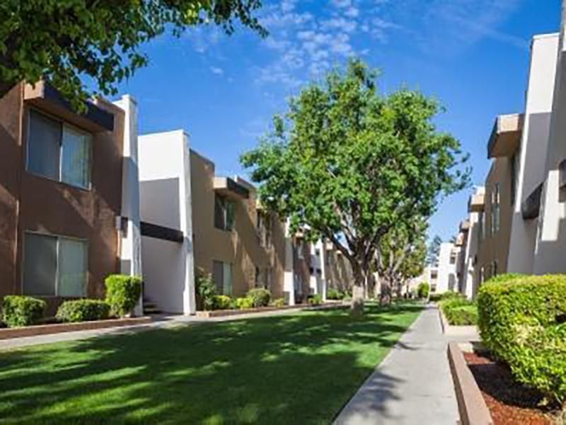 Apartment buildings with tan and white facades along a grassy walkway, under a blue sky.