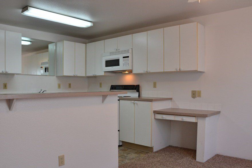White kitchen with overhead cabinets, microwave, stove, and a counter.