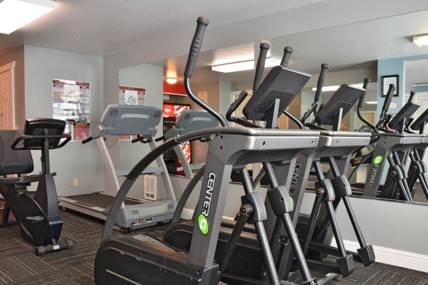 Gym with treadmills, elliptical machines, and stationary bikes. Mirrors reflect equipment.