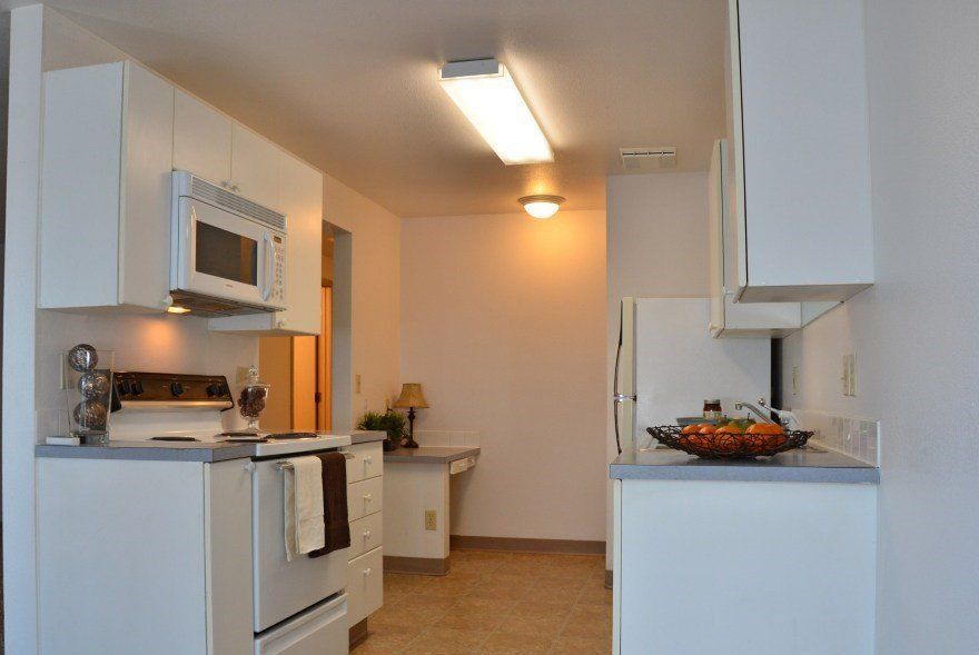 Small, white kitchen with appliances, cabinets, and a desk.