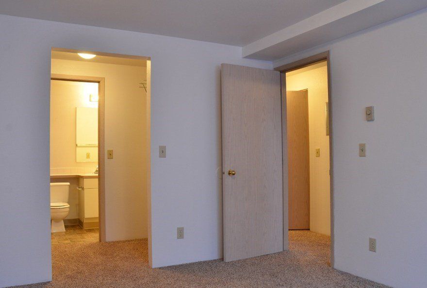 Interior view of a bedroom with three doorways: bathroom on the left, closet in the middle, and hallway on the right.
