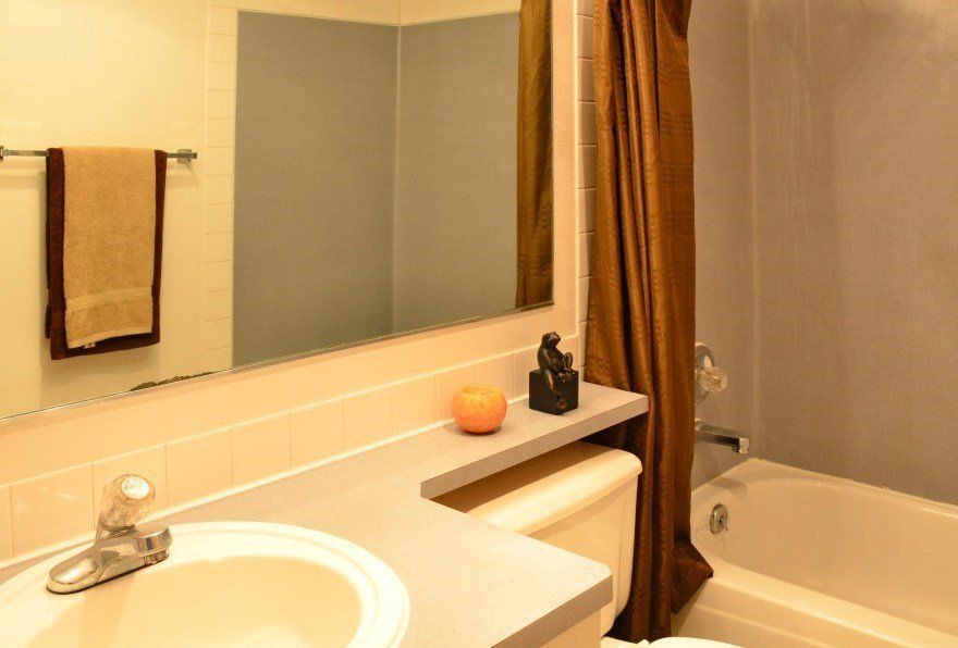 Bathroom with beige sink, toilet, and counter; tan towel; brown curtain; and mirror reflecting a gray wall.