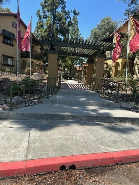 Entrance to apartment complex with a walkway, pergola, and flags.