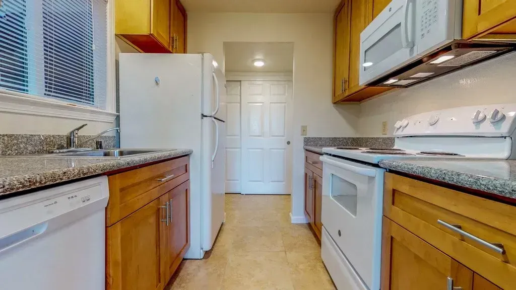 Kitchen with wooden cabinets, white appliances, granite countertops, and a window.