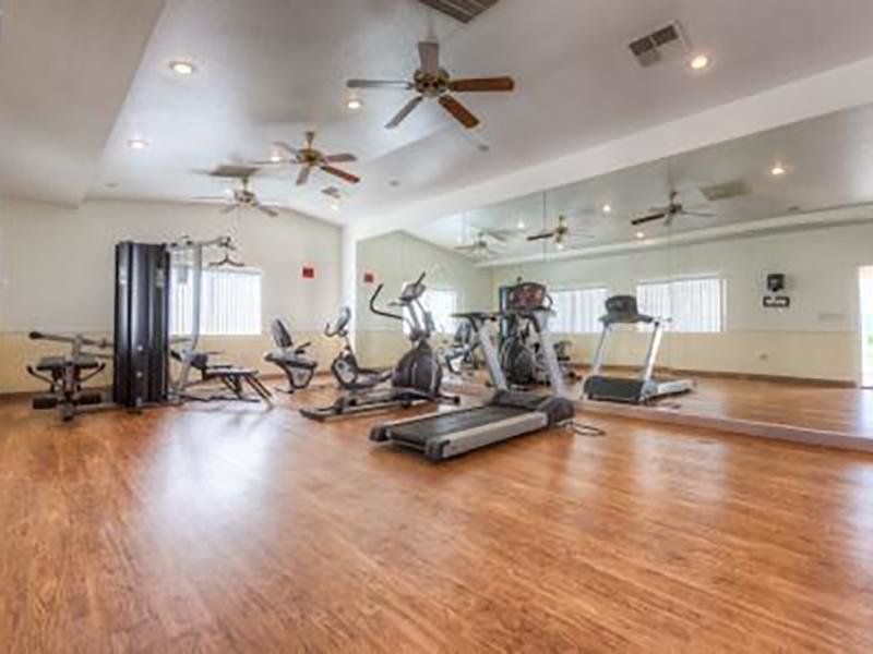 Gym with wooden floor, workout machines, large mirror, and ceiling fans.