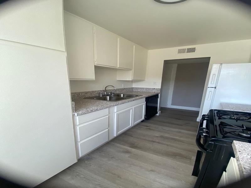 White kitchen with cabinets, countertops, sink, and gas stove. Gray flooring and walls.