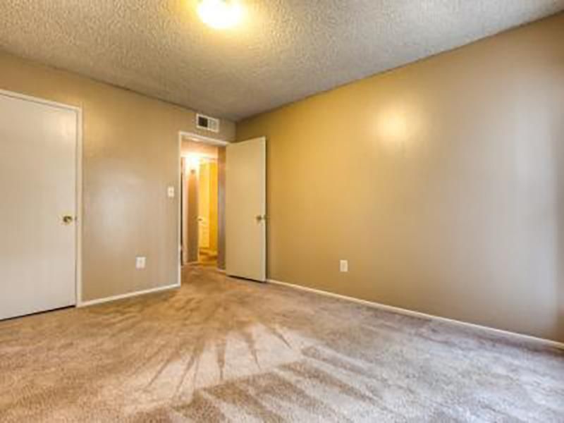 Empty bedroom with beige walls, two white doors, open doorway to hallway, and beige carpet.