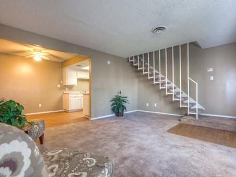 Living room with stairs, neutral colors, and partial view of kitchen.