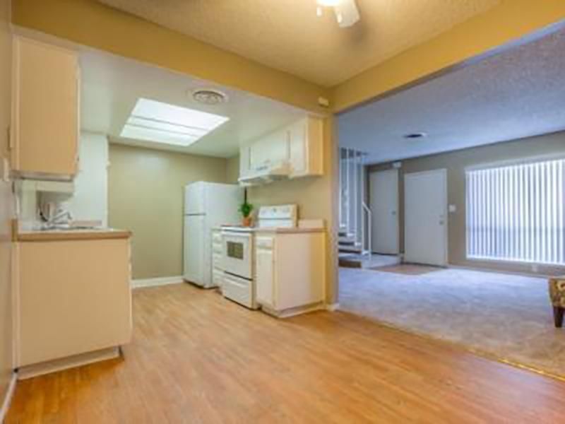 Kitchen with white cabinets, appliances, and wood-look flooring, opening to a carpeted living area.