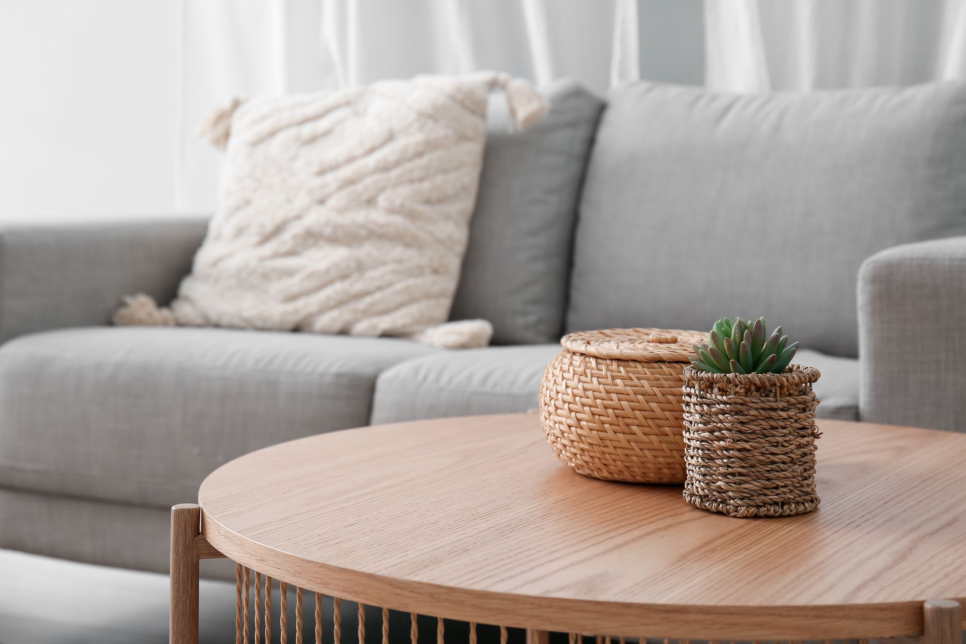 Wooden coffee table with basket and plant, in front of a gray couch with a textured pillow.